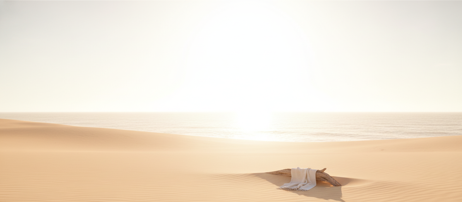 Coastal landscape at golden hour with warm amber light and a serene beach, hinting at a calm ocean under a bright white sky.